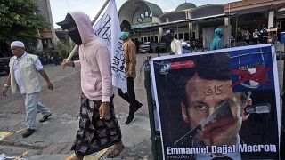 Manifestantes pasan junto a un cartel desfigurado de Emmanuel Macron en Medan, Indonesia