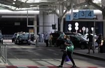 A woman wearing a face mask walks outside Lisbon's airport while in the background taxi drivers stand idle waiting for passengers, Friday, Sept. 11, 2020. Portugal