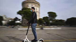 A man wearing a face mask against the spread of the coronavirus, rides an electric scooter in front of the White Tower