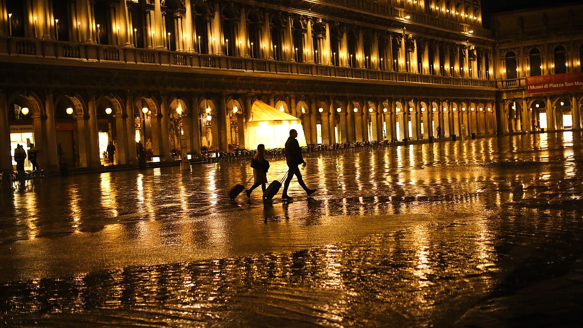 Tourists pull their luggage as they walk through a nearly empty St. Mark's Square on a rainy day in Venice, Monday, March 2, 2020