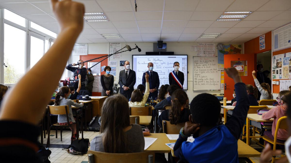 Children raise their hand as French Prime Minister Jean Castex, second left, and Education Minister Jean-Michel Blanquer, second right, attend a homage to Samuel Paty. 