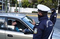 A policeman, wearing a face mask to protect against coronavirus, asks a passenger of a car to display his movement permission form