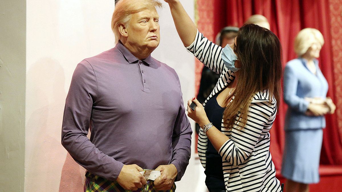 A member of the Madame Tussauds studios team places a set of golf clubs next to a wax figure of US President Donald Trump which has been re-dressed in golf wear.