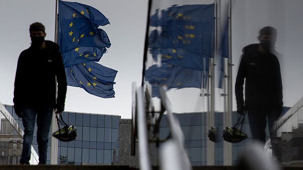 A man carries a cycling helmet as he walks by EU flags outside EU headquarters in Brussels, Wednesday, Oct. 28, 2020. A man carries a cycling helmet as he walks by EU flags outside EU headquarters in Brussels, Wednesday, Oct. 28, 2020.