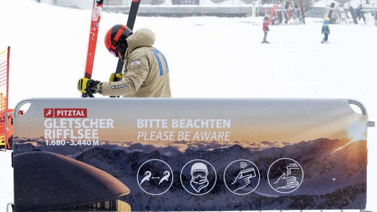 A skier prepares his skis next to the covid-19 safety instruction sign at Pitztal glacier, Austria 