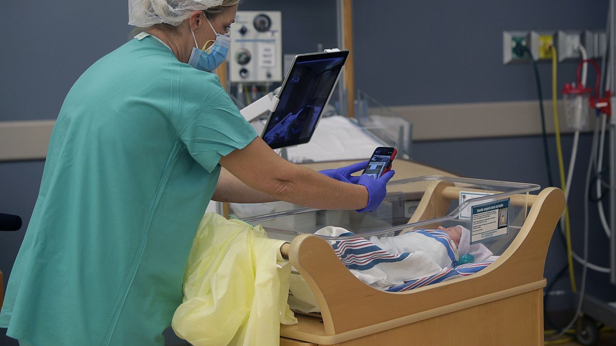 Медсестра фотографирует новорождённого для изолированной из-за Covid-19 матери