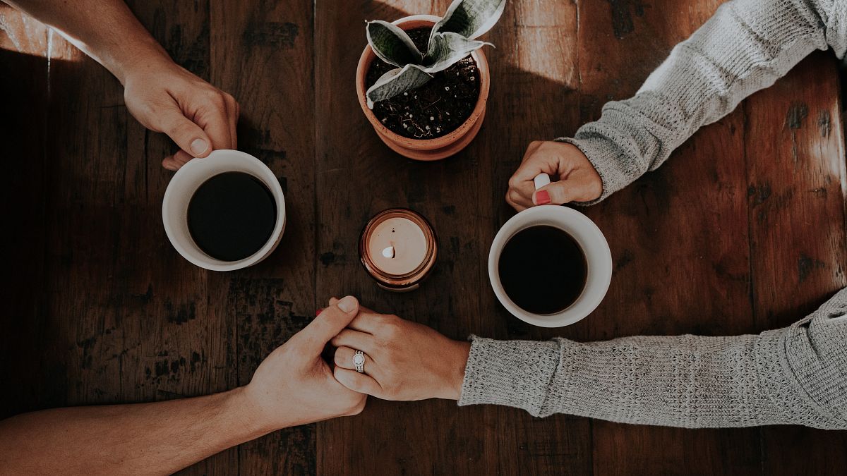 Una pareja se agarra de la mano con dos tazas de café