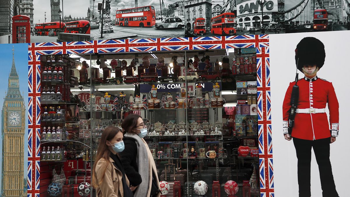 Shoppers walk past a shop window in Oxford Street, London, Tuesday, Oct. 13, 2020. 