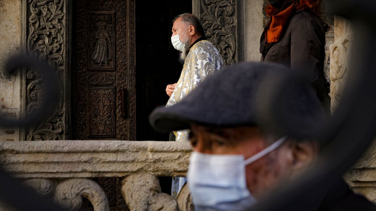 A priest wearing a mask for protection against the COVID-19 infection stands outside the Stavropoleos church, built in 1724, in Bucharest, Romania, Sunday, Nov. 8, 2020