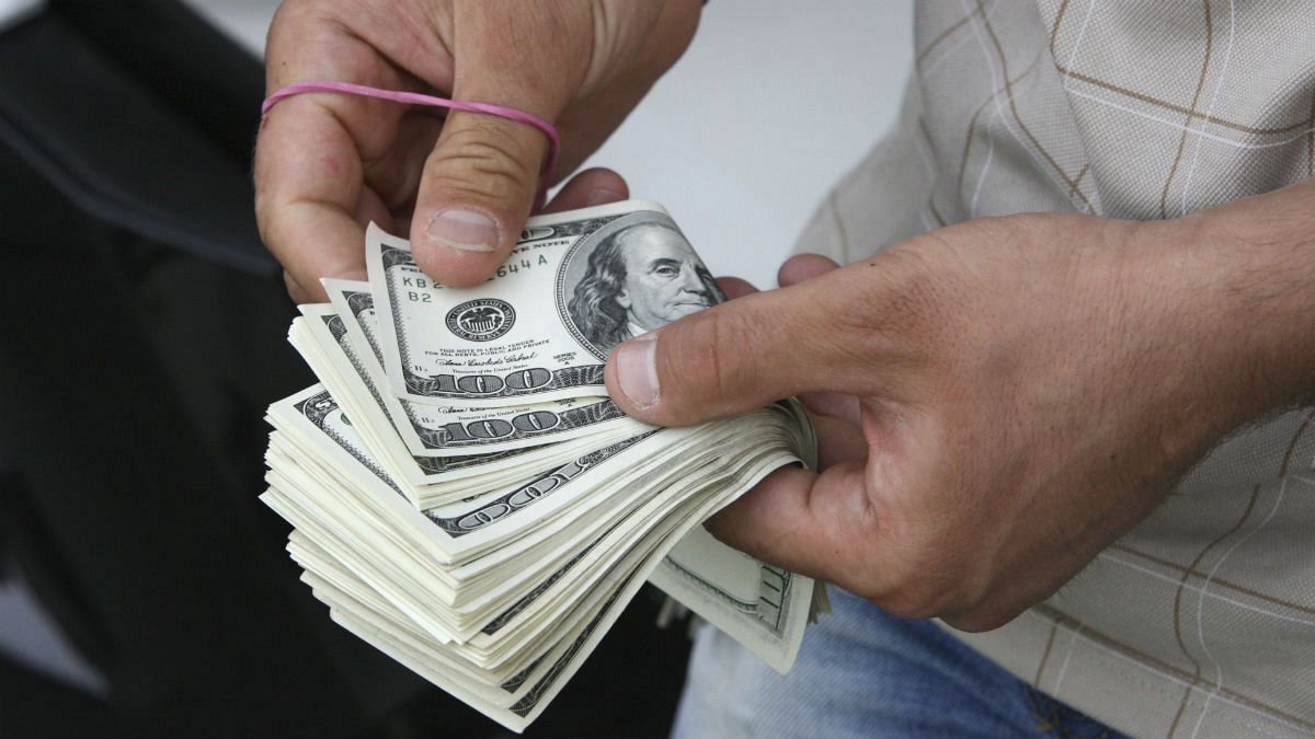 شمارش اسکناس‌های دلار توسز یک فروشنده ارز در بازار تهران