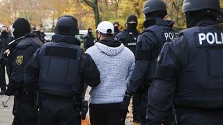 Police officers escort a person for an identity check in Berlin, Germany, Tuesday, Nov. 17, 2020.