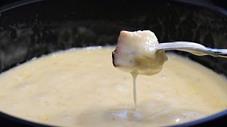 A diner dips bread into a "caquelon" pot containing melted cheese and wine.