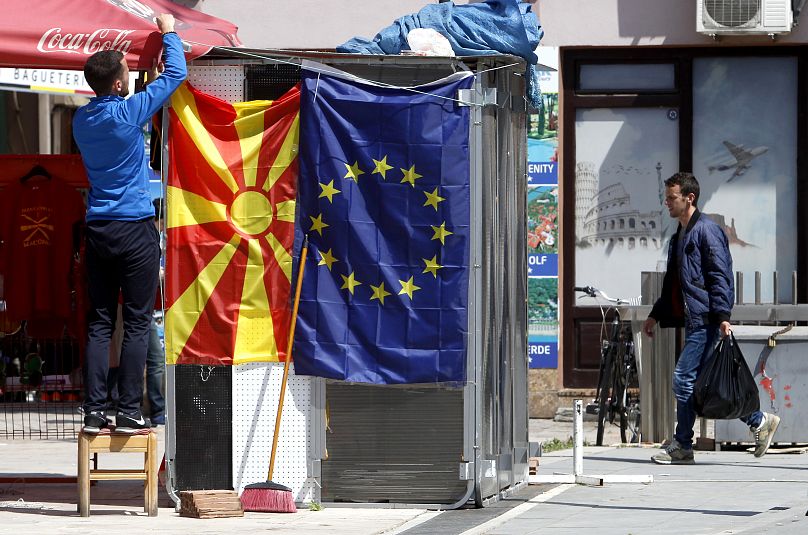 Um vendedor ambulante fixa a bandeira da Macedónia do Norte ao lado de uma bandeira da UE numa rua em Skopje, 3 de maio de 2019