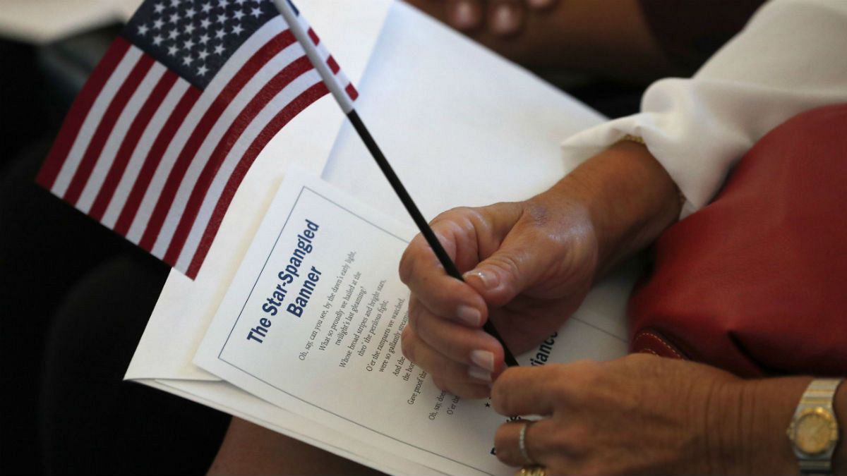 یک نامزد شهروندی با در دست داشتن پرونده خود و پرچم آمریکا در انتظار شروع مراسم اعطای تابعیت است