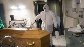 A worker, wearing a full protective equipment, disinfects the casket of someone who died of coronavirus COVID-19 at a funeral home in Charleroi, Belgium, Nov 17, 2020.