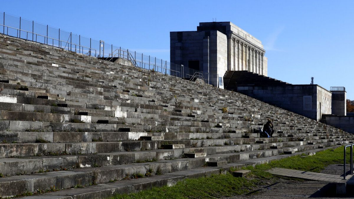 People sit on stairs at the 'Zeppelinfeld' besides the main tribune of the 'Reichsparteigelande' (Nazi Party Rally Grounds) in Nuremberg, Germany, Wednesday, Nov. 18, 2020. 