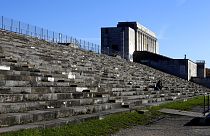 People sit on stairs at the 'Zeppelinfeld' besides the main tribune of the 'Reichsparteigelande' (Nazi Party Rally Grounds) in Nuremberg, Germany, Wednesday, Nov. 18, 2020.