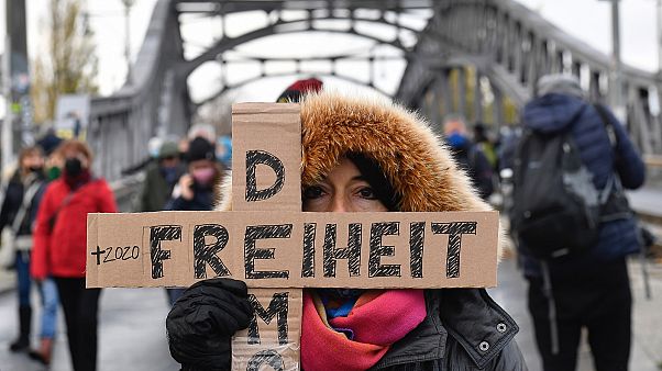 A woman attending a silent march against measures to curb the spread of coronavirus holds a cross reading "Freedom democracy" in Berlin on November 22, 2020. A woman attending a silent march against measures to curb the spread of coronavirus holds a cross reading "Freedom democracy" in Berlin on November 22, 2020.