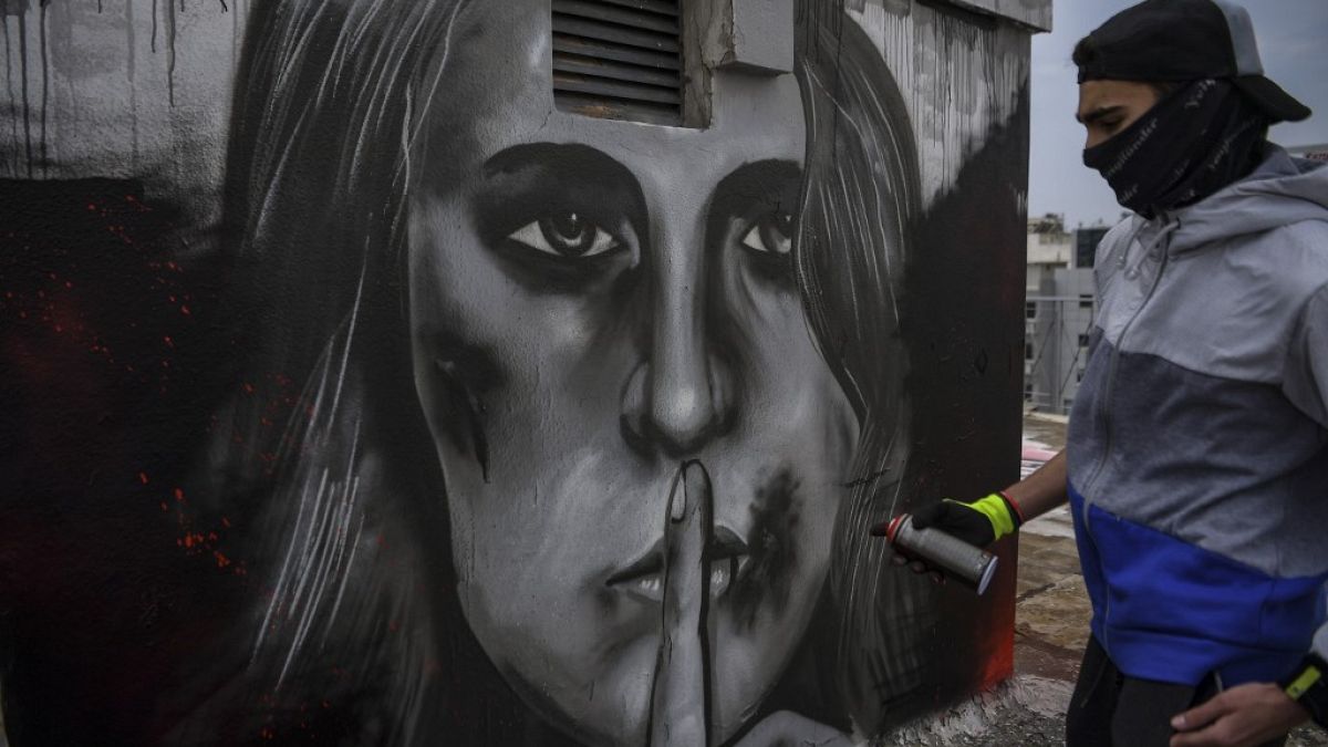  لوحة غرافيتية على سطح مبنى في أثينا، امرأة مصابة بجروح في وجهها وإصبعها على شفتيها، مستوحاة من زيادة حالات العنف المنزلي