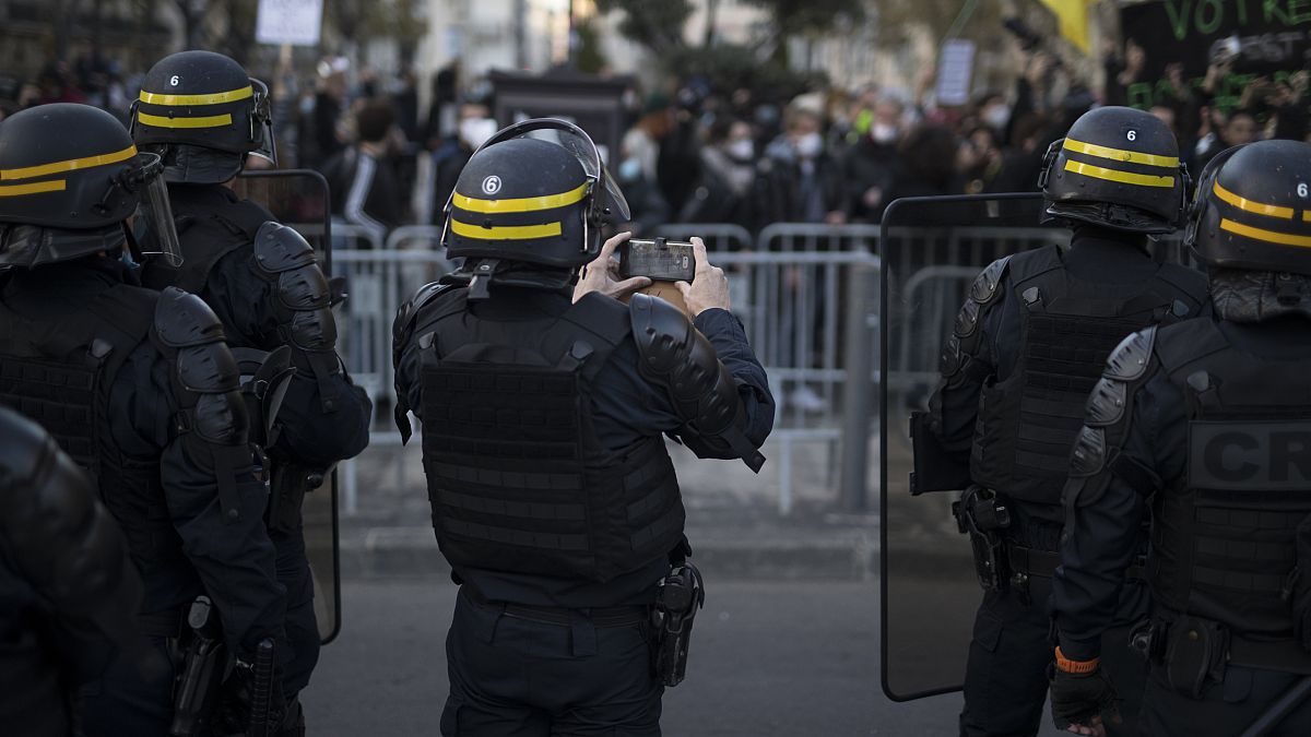 A French riot police officer photographs protesters with his phone during a demonstration in Marseille, southern France, Saturday, Nov. 21, 2020.