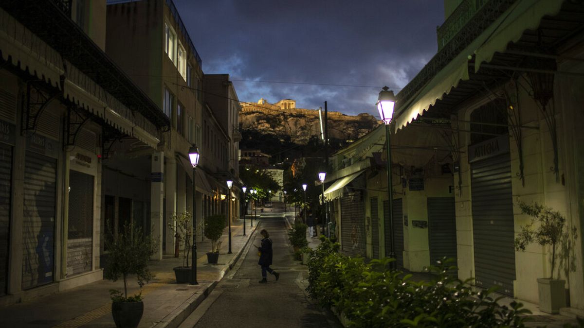 A woman walks on an empty street Plaka district of Athens with a part of the ancient Erechtheion temple on the Acropolis