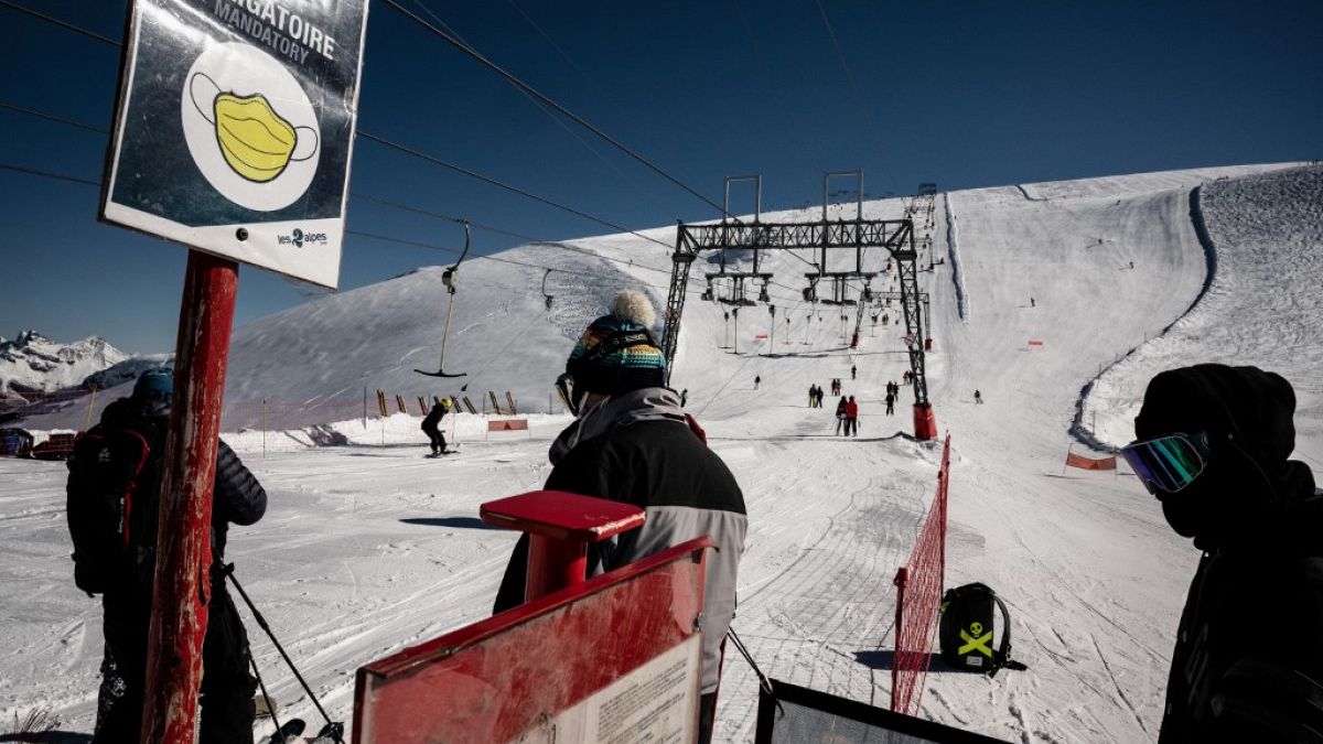 People wearing protective face masks queue up to use ski lifts, on the opening day of the Les 2 Alpes French resort on October 17