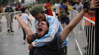 Mourners embrace as they wait to see Diego Maradona lying in state outside the presidential palace in Buenos Aires, Argentina, Thursday, Nov. 26, 2020.