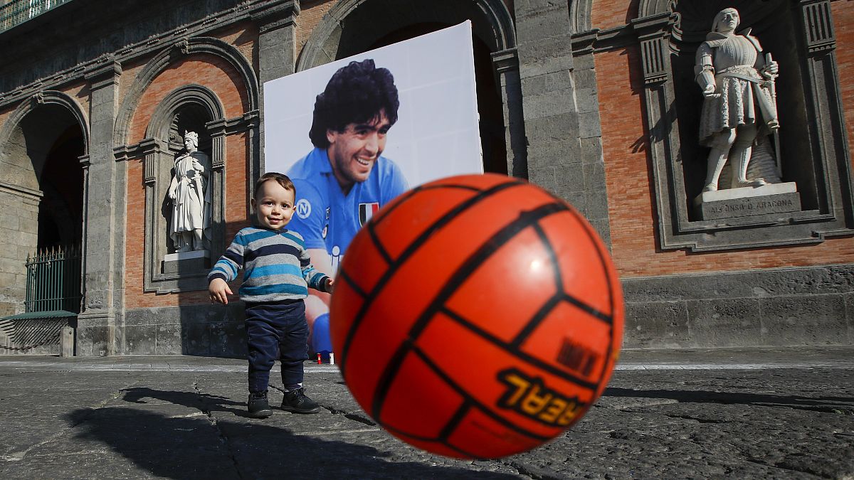 A child plays with a football in front of Naples' Royal Palace, which has a photo of Maradona hanging on it. Nov. 27, 2020.
