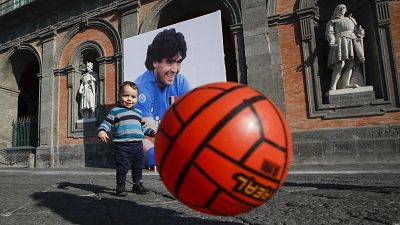 A child plays with a football in front of Naples' Royal Palace, which has a photo of Maradona hanging on it. Nov. 27, 2020.