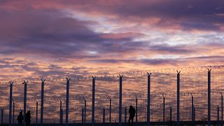 Migrants stand at a fence preventing them from reaching a highway beside the migrant camp known as the Jungle in Calais, northern France, Tuesday, Nov. 3, 2015
