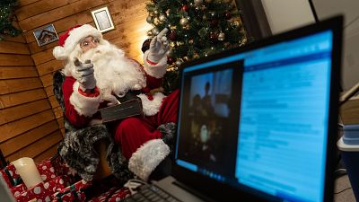 Aaron Spenedelow dressed as Santa Claus waves to the camera during a Zoom call with a family