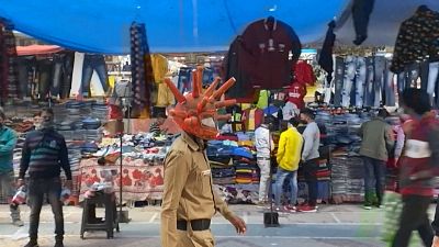 Policeman wearing a virus-shaped helmet walks around a busy market