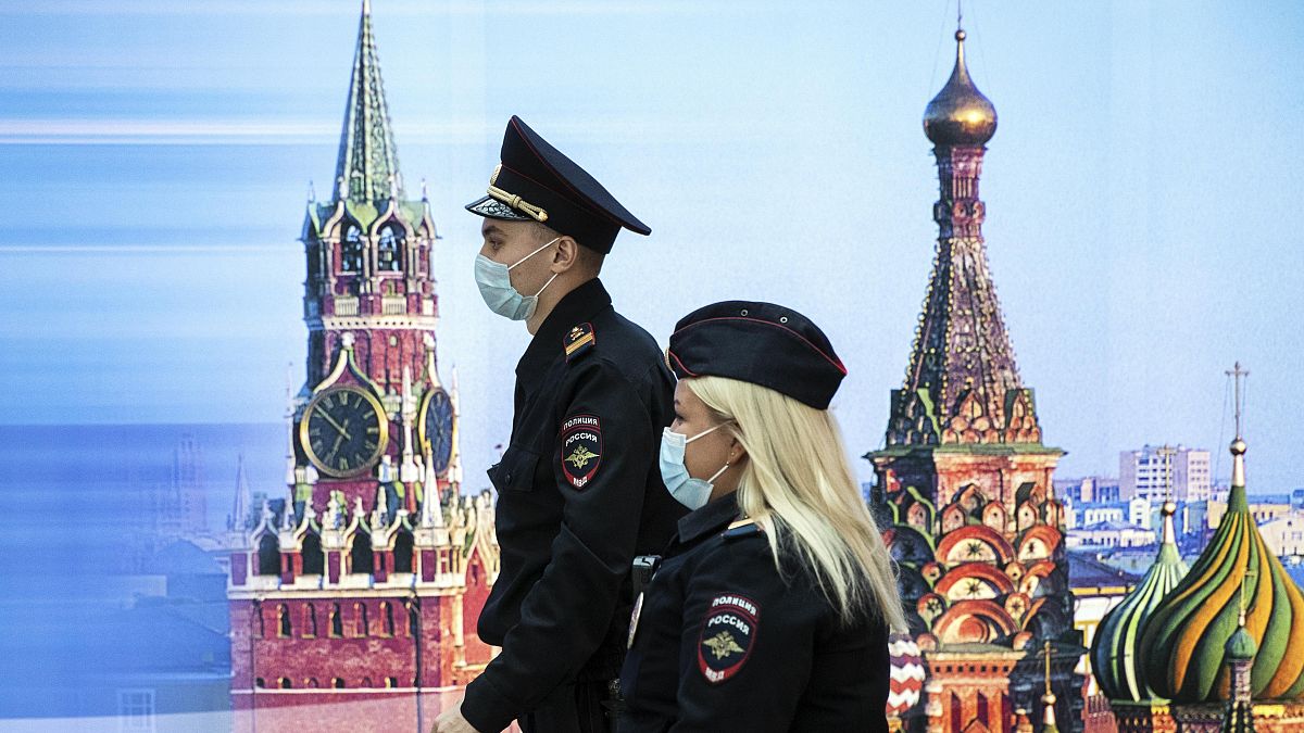 Сотрудники полиции идут мимо фотографии Спасской башни и Собора Василия Блаженного в аэропорту Шереметьево