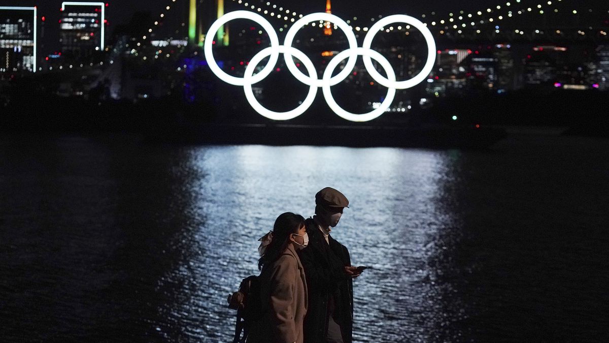 رجل وامرأة يمشيان حذو شعار الأولمبياد العائم في طوكيو. 2020/12/01