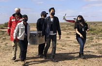 Miembros del Organismo de Exploración Aeroespacial de Japón cargan una caja que contiene muestras de asteroides que recuperaron en el sur de Australia tras su aterrizaje.