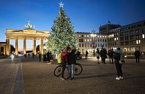 People gather in front of Germany's landmark Brandenburg Gate with the illuminated Christmas tree at the Pariser Platz square in Berlin, Germany, Monday, Dec. 7, 2020.