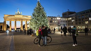 People gather in front of Germany's landmark Brandenburg Gate with the illuminated Christmas tree at the Pariser Platz square in Berlin, Germany, Monday, Dec. 7, 2020.