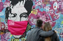  couple look at the Lennon Wall with a face mask attached to the image of John Lennon