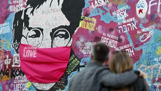 A couple look at the "Lennon Wall" with a face mask attached to the image of John Lennon, in Prague, Czech Republic, on April 6, 2020