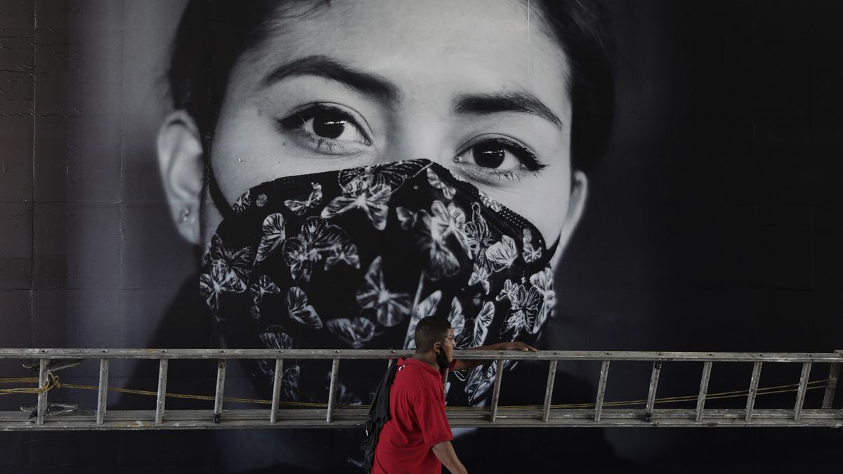 Un hombre pasa por delante de un cartel que invita a llevar mascarilla, Ciudad de México