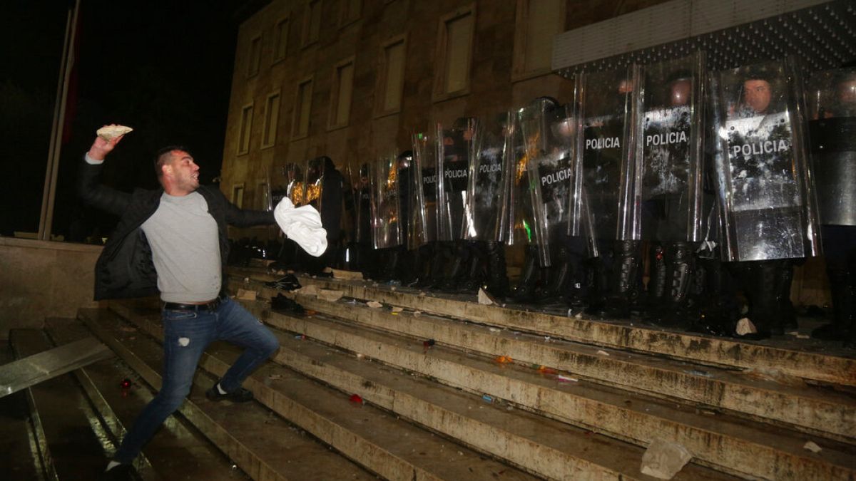 A protester throws a stone to police officers outside the Prime's Minister office during clashes in Tirana, Albania , on Wednesday, Dec. 9, 2020