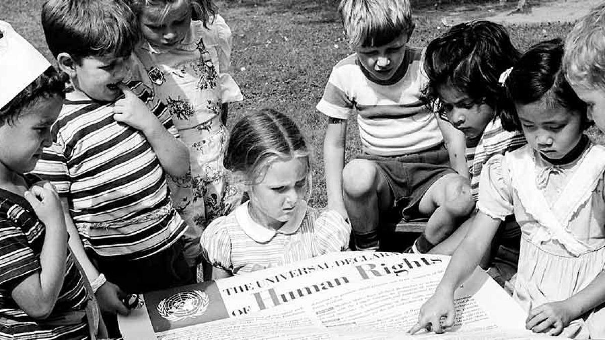 أطفال من الحضانة الدولية التابعة للأمم المتحدة ينظرون إلى ملصق للإعلان العالمي لحقوق الإنسان. (1950) ©الأمم المتحدة