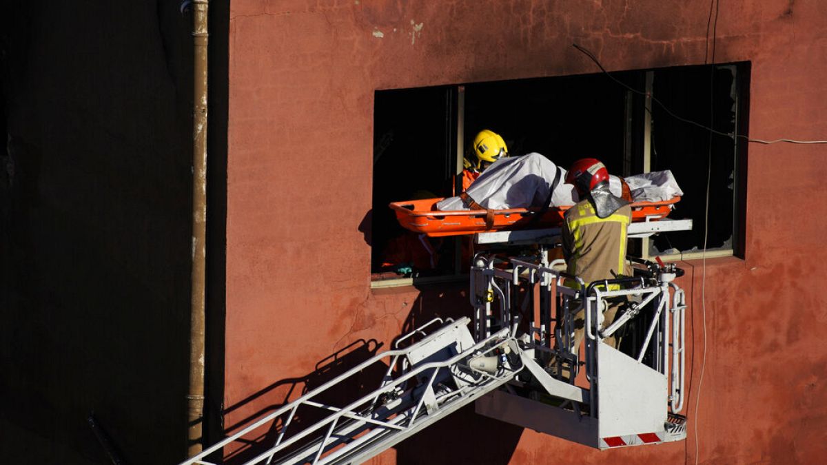 Firefighters load the body of a dead person into a crane after a fire on a building in Badalona, Barcelona, Spain, 