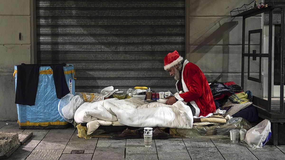 Un senzatetto, di nome Rafael, indossa un abito da Babbo Natale mentre si prepara a cenare sul ciglio di una strada, a Milano, giovedì 10 dicembre 2020
