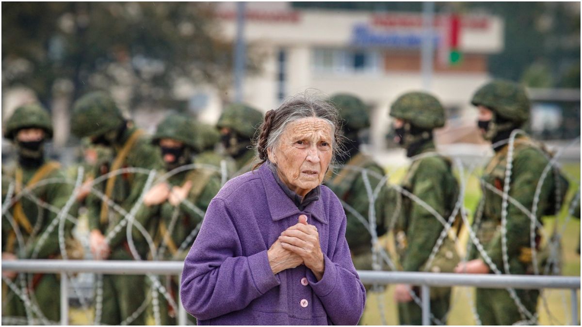 سيدة مسنة تمشي خلف جنود يقفون قبالة سياج شائكة أثناء مظاهرة في مينسك، بيلاروسيا. آب-أغسطس