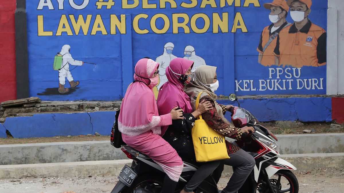 Muslim women ride a motorbike past a coronavirus-themed mural in Jakarta, Indonesia, Thursday, Sept. 10, 2020. Writings on the mural read "Let's fight coronavirus together"
