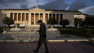 A man wearing a protective mask to curb the spread of the coronavirus walks in front of the Athens University building