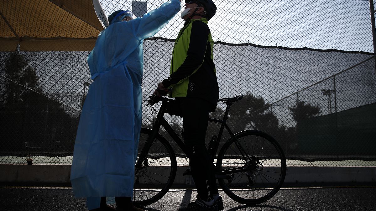 A medical staff member of the National Health Organization (EODY) conducts a COVID-19 rapid test on a bicycle rider at a drive-through testing site in Athens