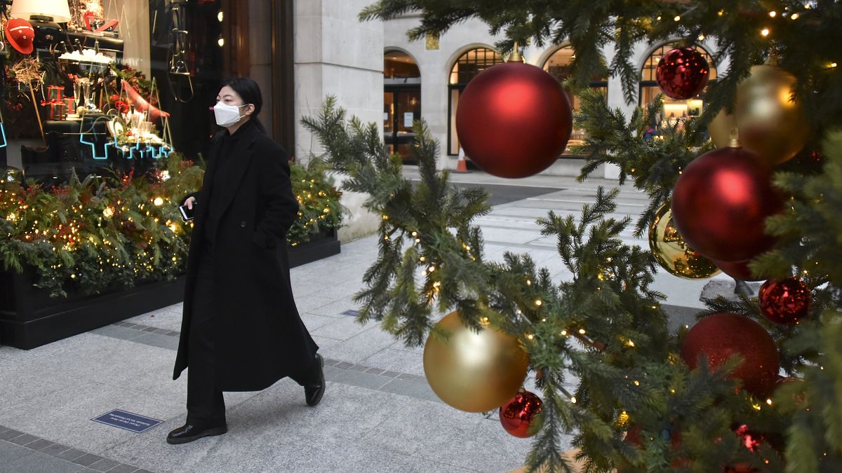 A woman wears a face mask as she walks past a Christmas tree in New Bond Street, in London, Tuesday, Dec. 22, 2020.
