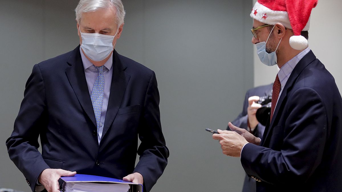 A collegue wears a Christmas hat as EU chief negotiator Michel Barnier, left, carries a binder of the Brexit trade deal during a special meeting in Brussels, Dec 25, 2020.